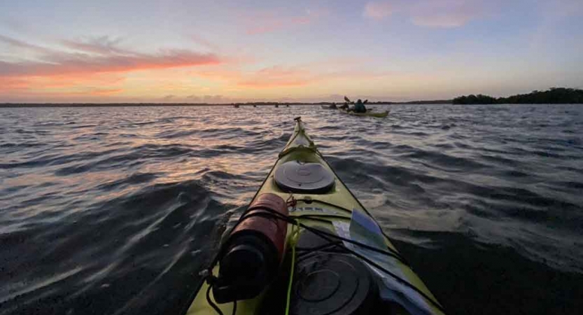 a kayak points to the sun as its sets over water